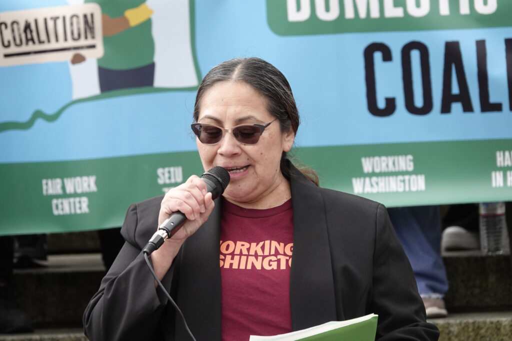 A woman in a Working Washington shirt giving a speech at a rally.